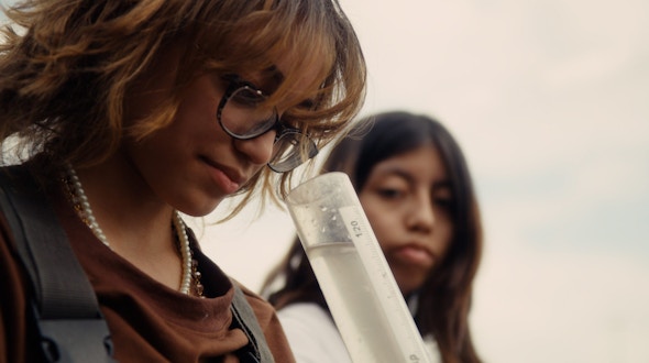Girl wearing glasses looking down into tube filled with water.