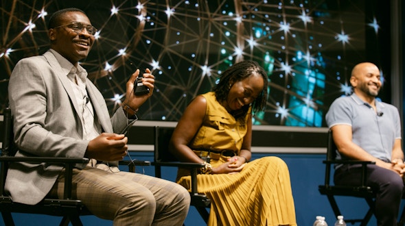 Two men and a woman sitting in chairs and talking to a crowd.