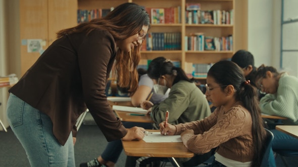 Female teacher standing in front of class and helping one of the students