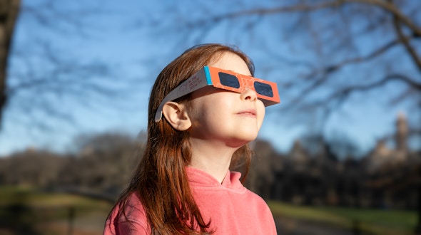 Photo of little girl wearing a hoodie and eclipse glasses