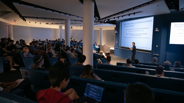 Man holding a pointer who is lecturing in front of a full room.