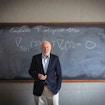 Jim stands in front of a chalkboard. A mathematical equation is written on the board.