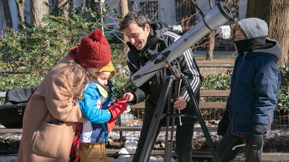 Three people looking through a telescope in a park