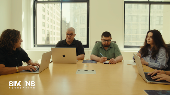 A group of people sitting around a table with computers in front of them